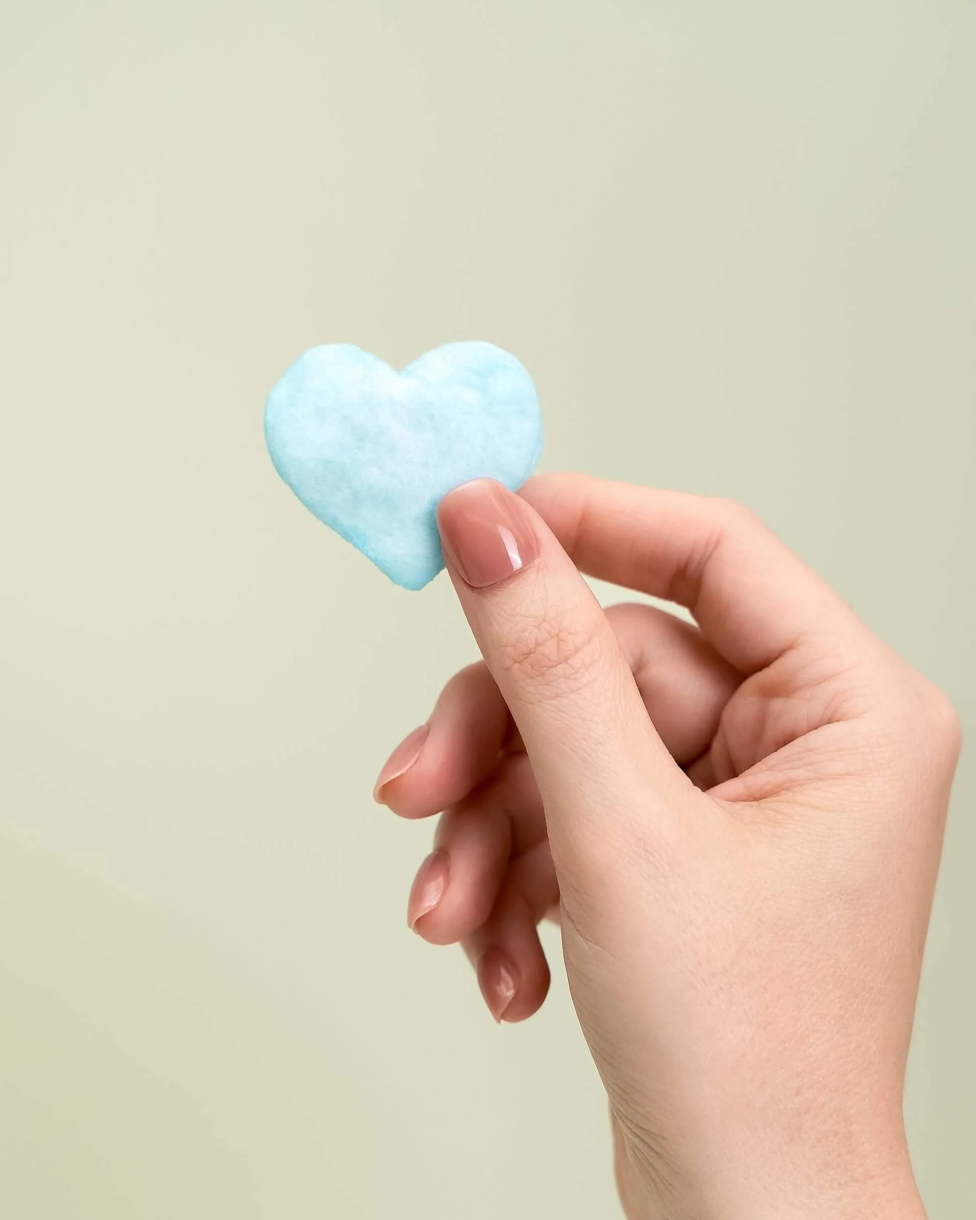 A hand holds a blue cotton candy heart in front of an olive green background