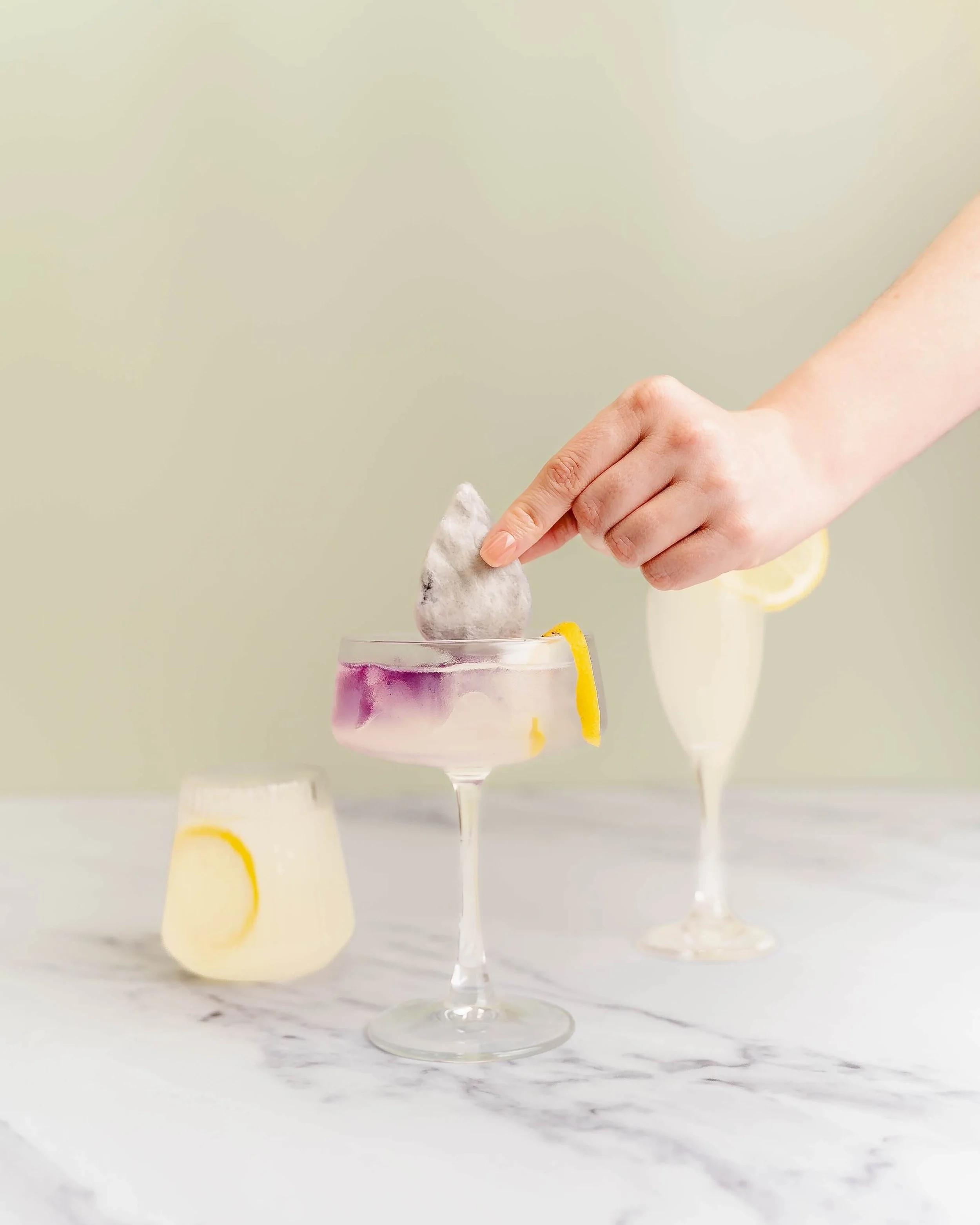 A hand dips a drink drop into a cocktail glass of lemonade