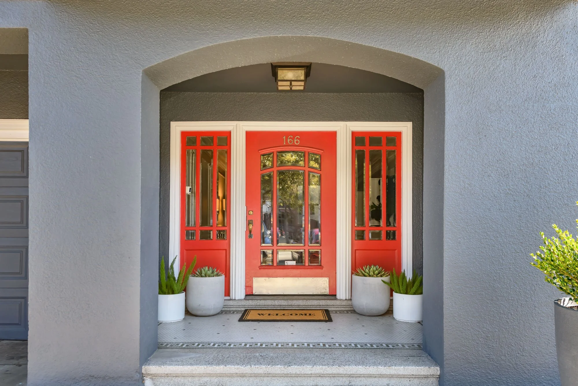 Red front door with glass panels, house number 166, white trim, potted plants, and a welcome mat.