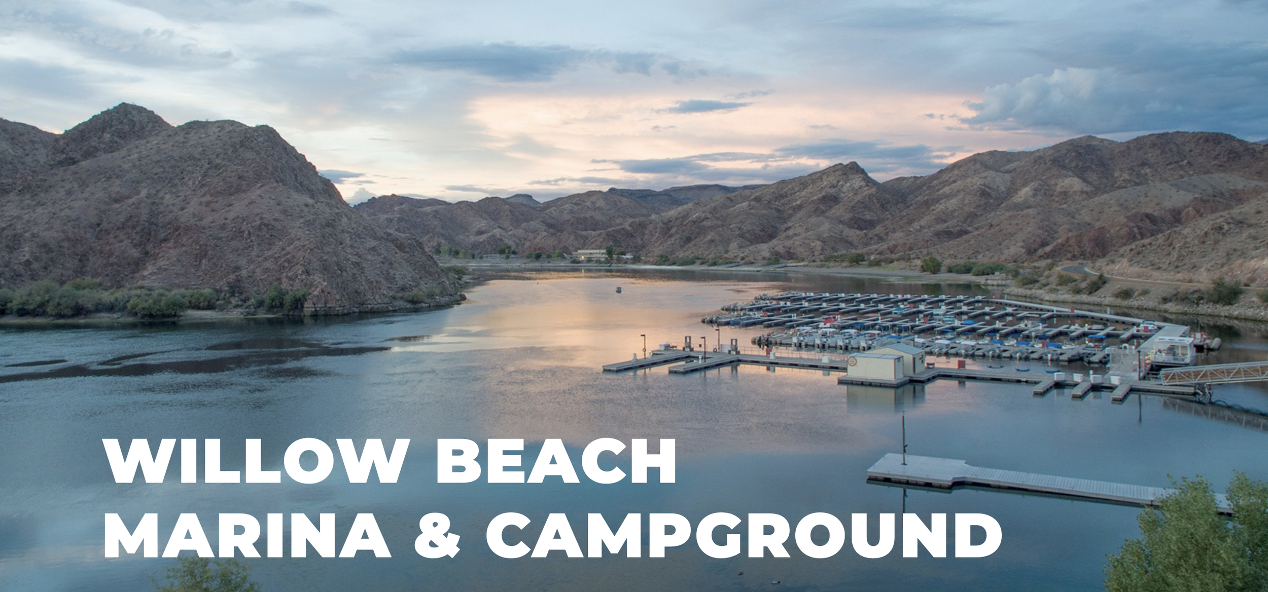A scenic view of Willow Beach Marina and campground with a calm river, dock, and mountain hills in the background during sunset.