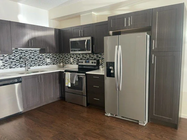 Sparkling clean kitchen after a deep clean by AAE Home Glow, featuring marble backsplash, black cabinets, and stainless steel appliances in a Calgary home..
