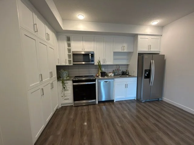 Sparkling clean kitchen after a deep clean by AAE Home Glow, featuring marble backsplash, black cabinets, and stainless steel appliances in a Calgary home.