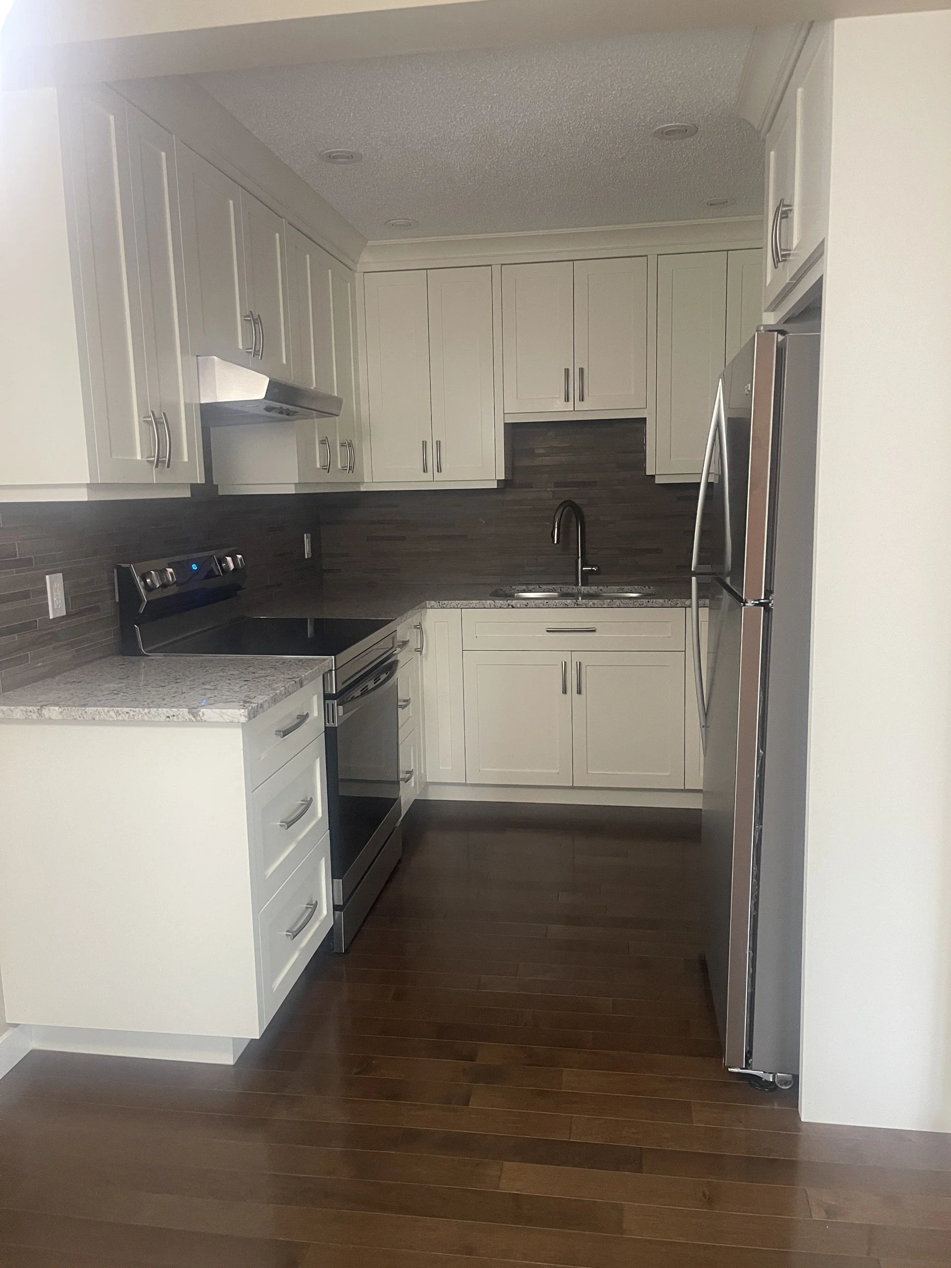 Sparkling clean kitchen after a deep clean by AAE Home Glow, featuring marble backsplash, black cabinets, and stainless steel appliances in a Calgary home.