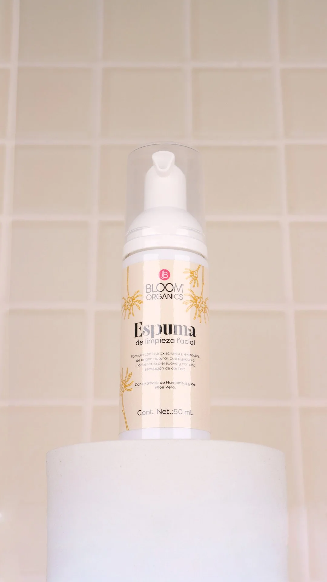 Botella de espuma de limpieza facial con etiquetas en español, sobre un soporte blanco, fondo de azulejos beige.