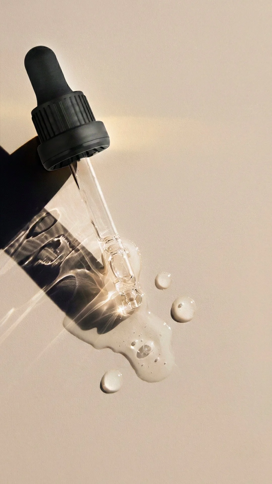 Un gotero de plástico negro con líquido que se cae, formando gotas en una superficie clara.