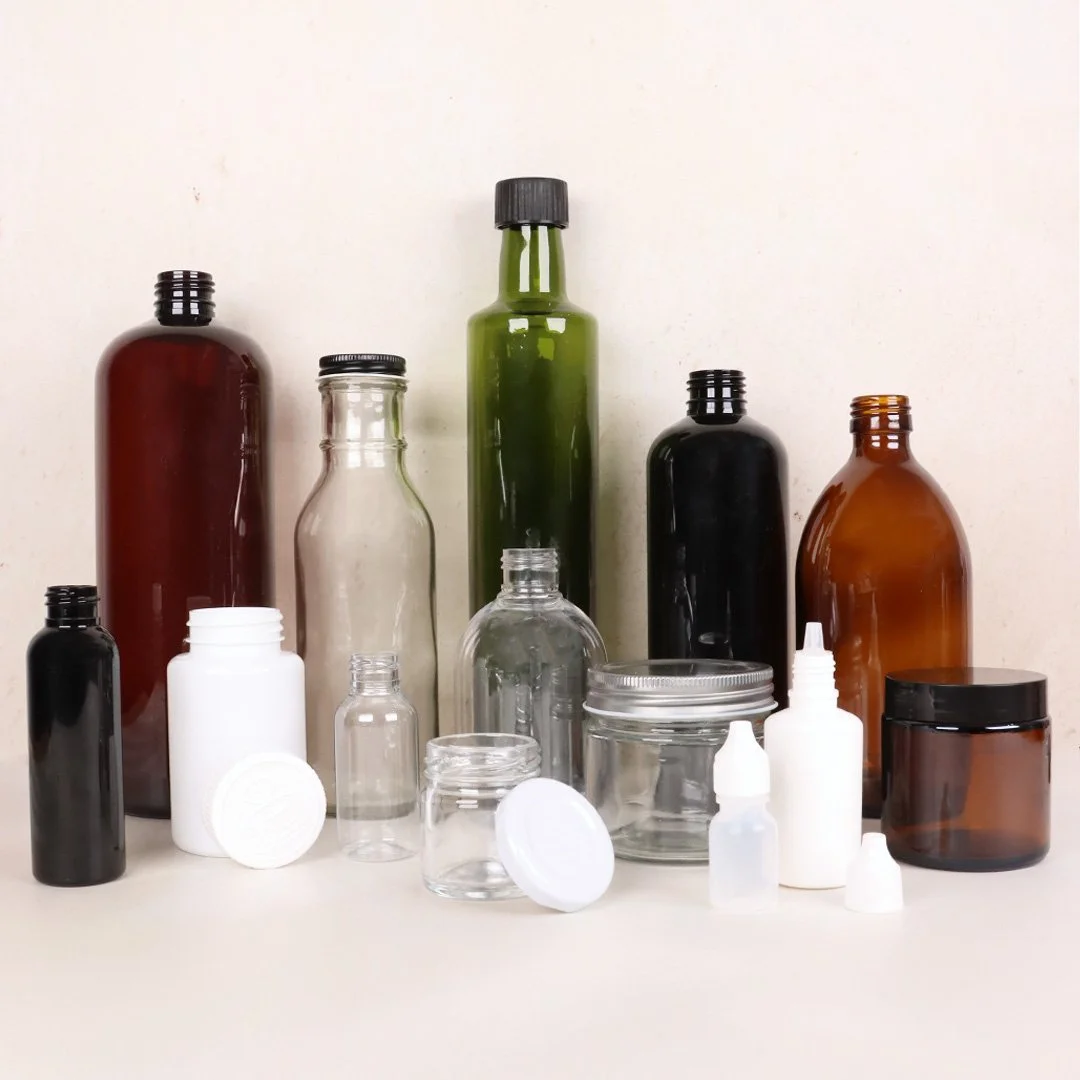 varios frascos y botellas de diferentes tamaños y colores, incluyendo vidrio y plástico, algunos con tapas y otros sin, sobre una superficie clara