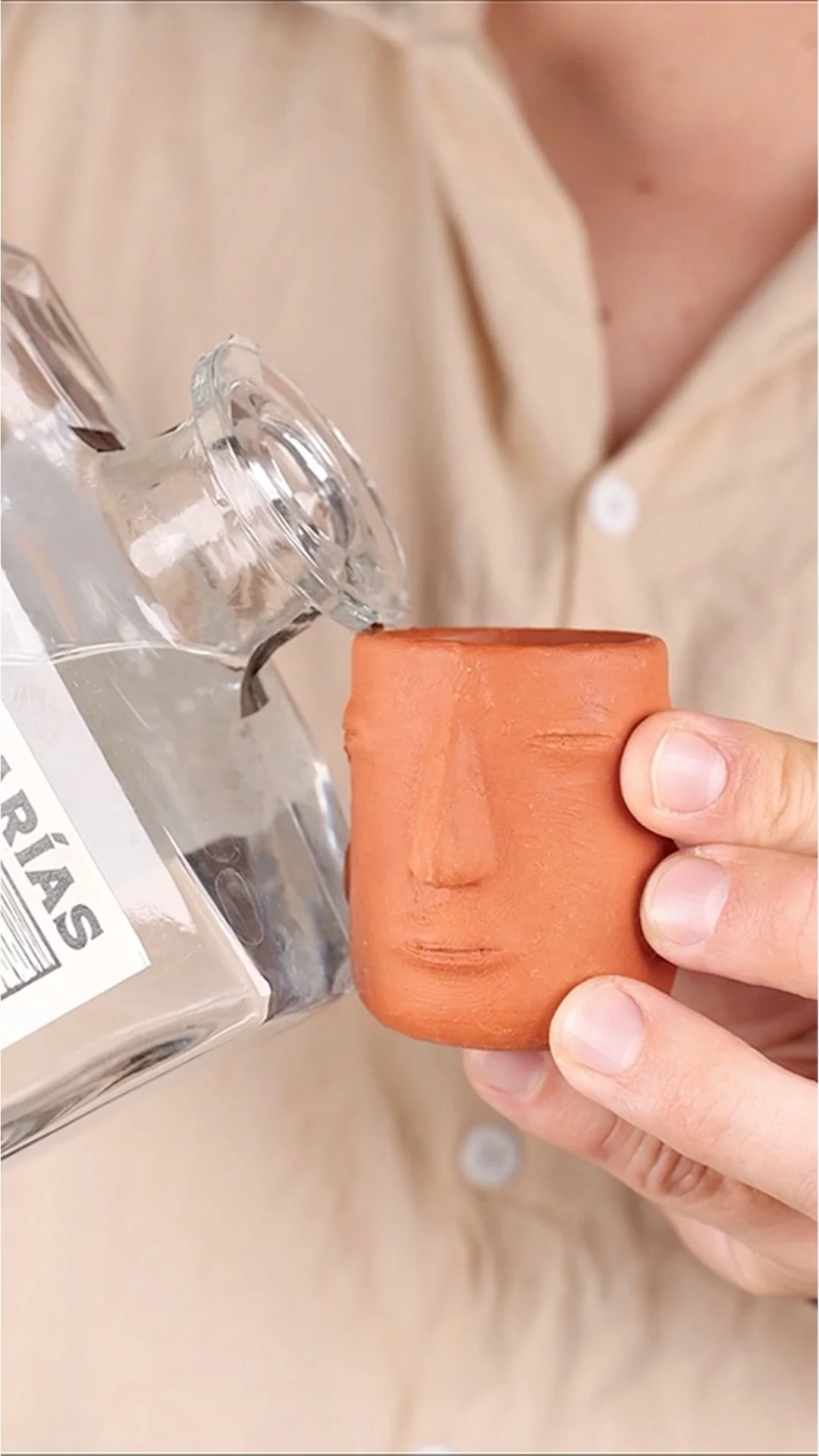 Una persona sostiene una taza de barro con forma de rostro humano mientras vierte agua en ella.