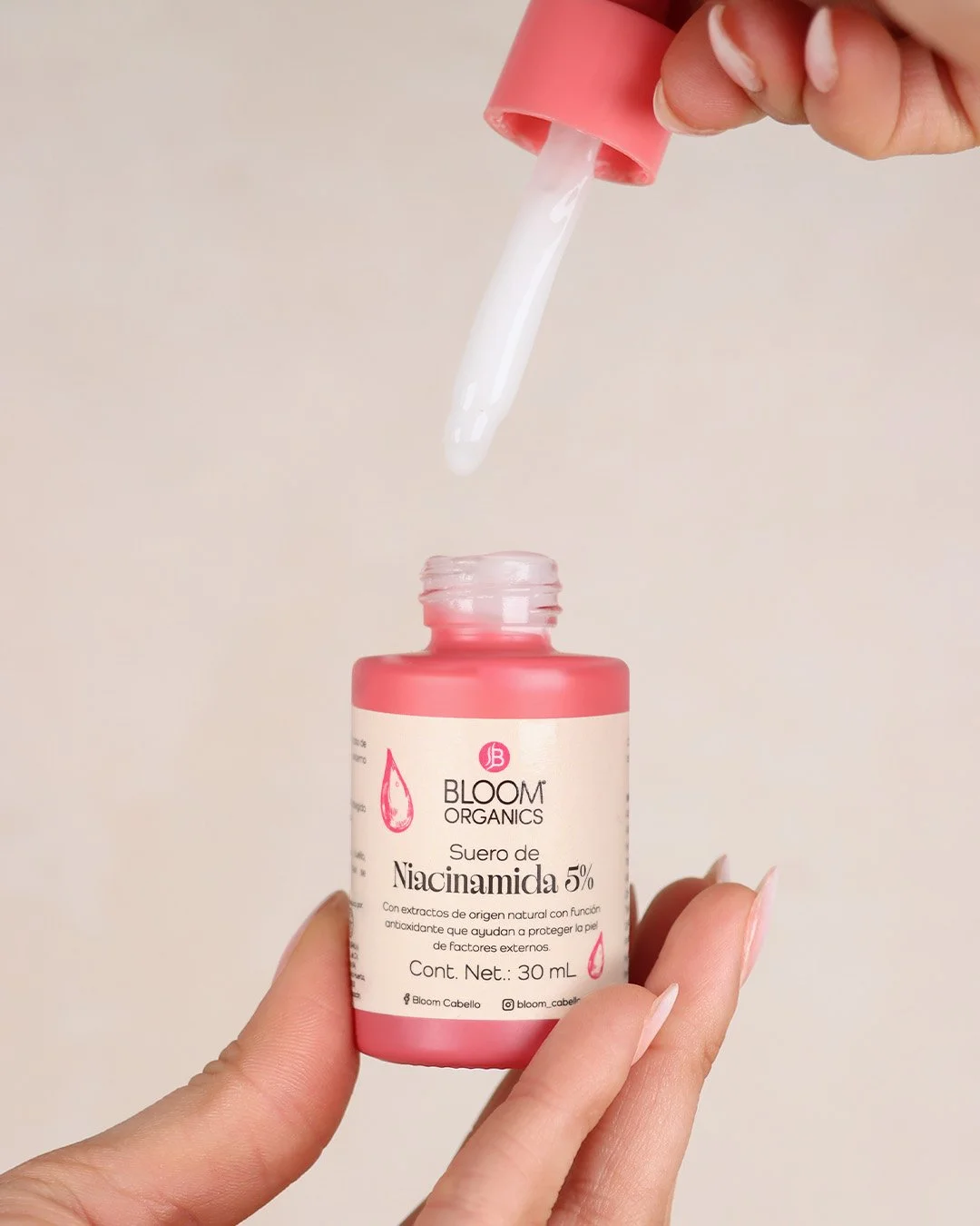 Mano sosteniendo un frasco de suero de Niacinamida al que se le ha retirado la tapa y la pipeta está en el aire con una gota de líquido. La etiqueta del frasco muestra que contiene 5% de Niacinamida y de la marca Bloom Organics.