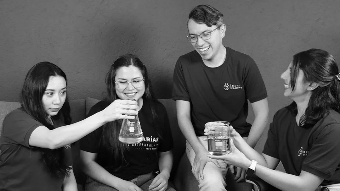 Cuatro jóvenes en un ambiente de laboratorio, compartiendo una actividad con líquidos en vasos medidores y frascos, sonriendo y conversando.