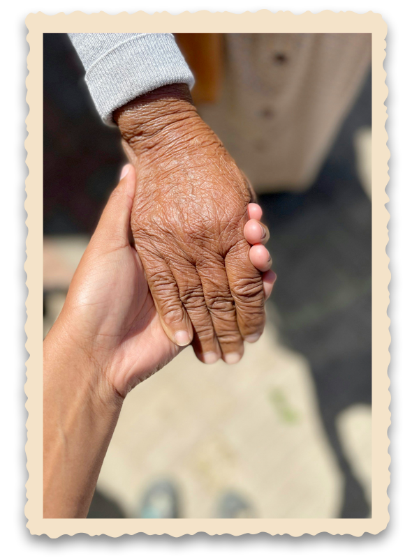 A younger person holding an elderly person's wrinkled hand with both hands.