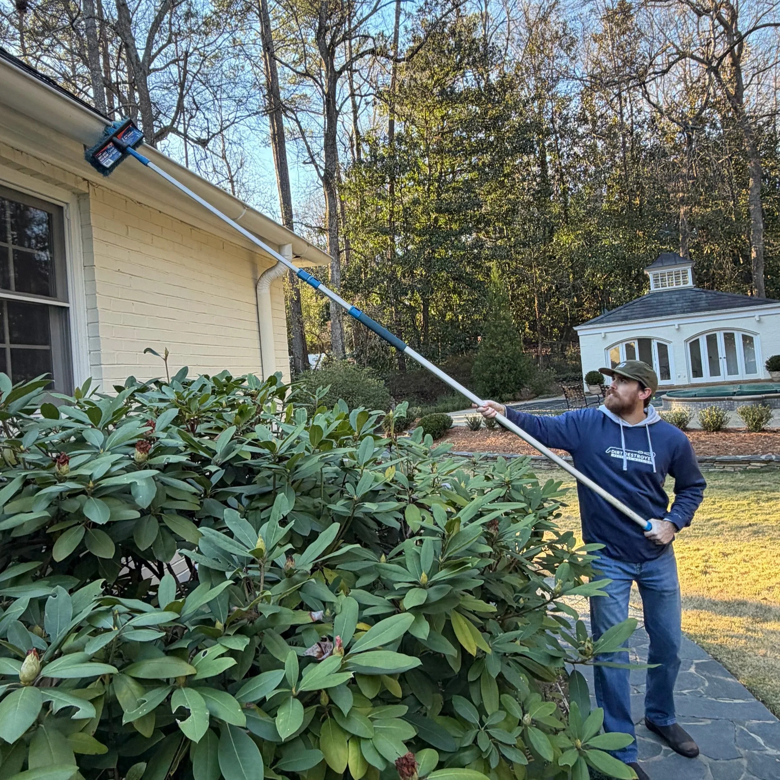 Man scrubbing stains out of the exterior of a metal gutter on a house on a sunny day.