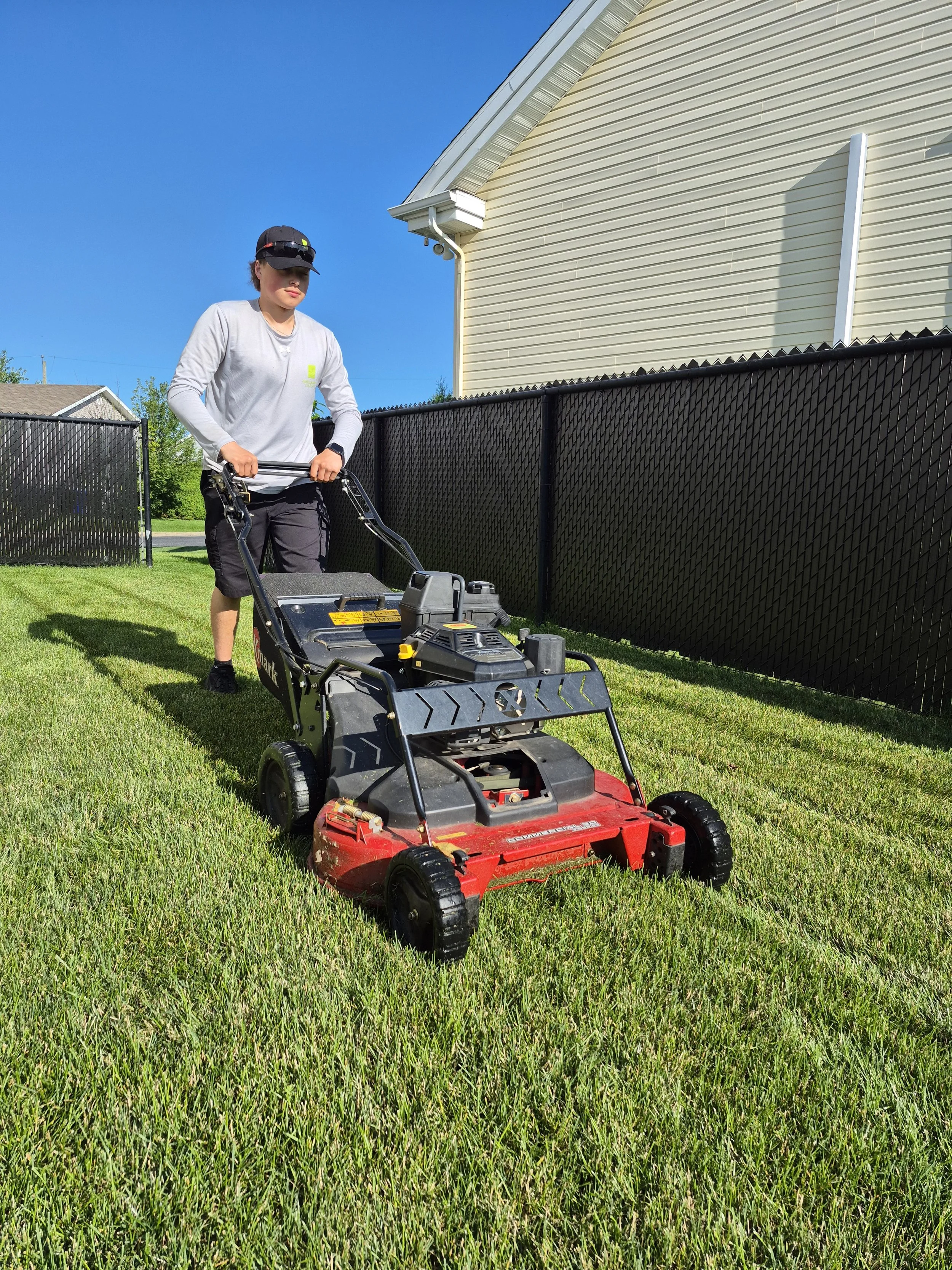 Une personne en train de tondre la pelouse à l'aide d'une tondeuse à gazon dans un jardin résidentiel ensoleillé.Nous offrons nos services de tonte de pelouse à , Sainte-Julie, Boucherville, Varennes et beloeil