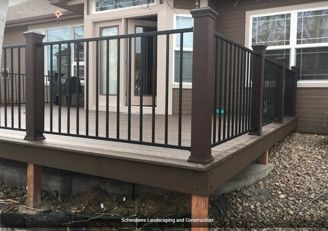 Newly built wooden deck with black metal railing in front of a house with beige siding and large windows