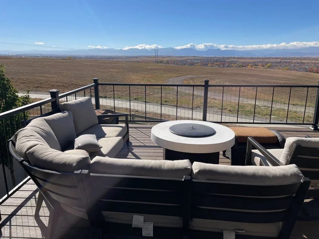 Outdoor patio with cushioned seating area and a view of open fields and distant front range colorado mountains under a blue sky.