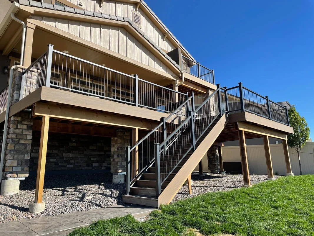 Newly built elevated wooden deck with black metal railing attached to the back of a house, featuring staircase leading down to a grassy yard.