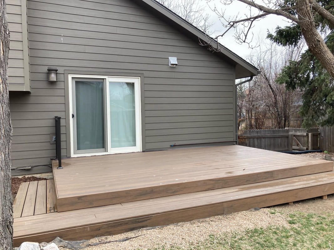 A newly built wooden deck attached to a house with gray siding and a sliding glass door. 