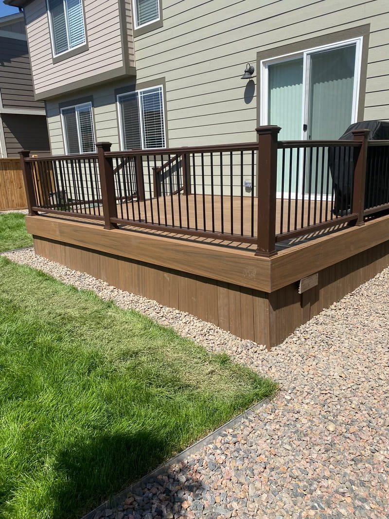 Backyard wooden deck with black railing, sliding glass door, and outdoor lighting