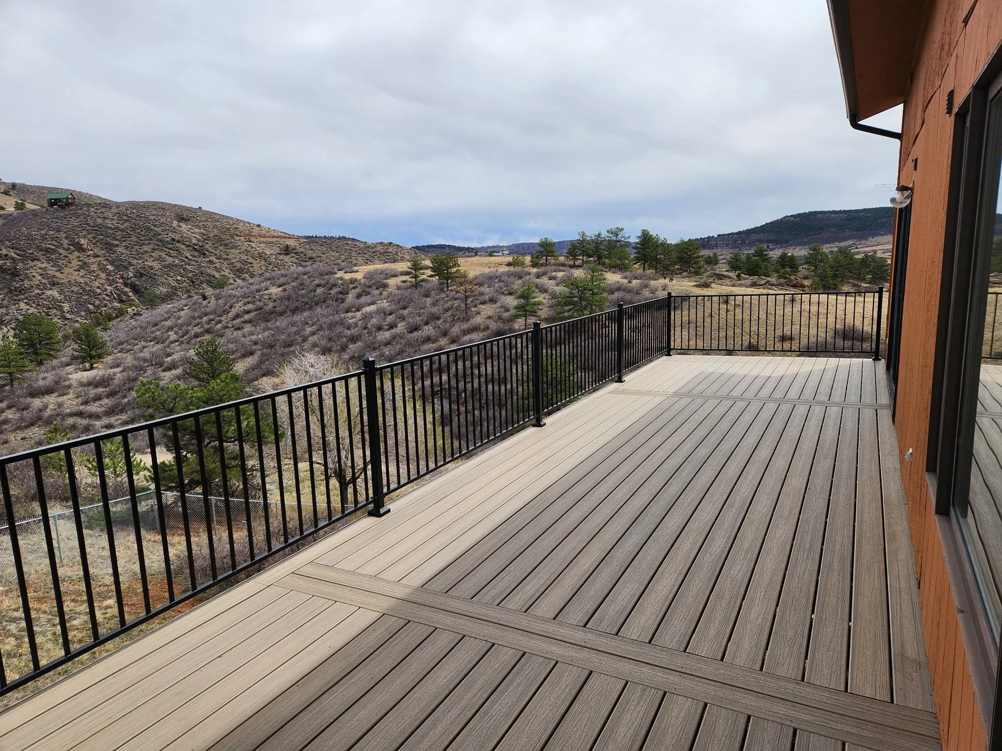 Colorado mountain composite wooden deck with black metal railing overlooking barren hills and sparse trees 