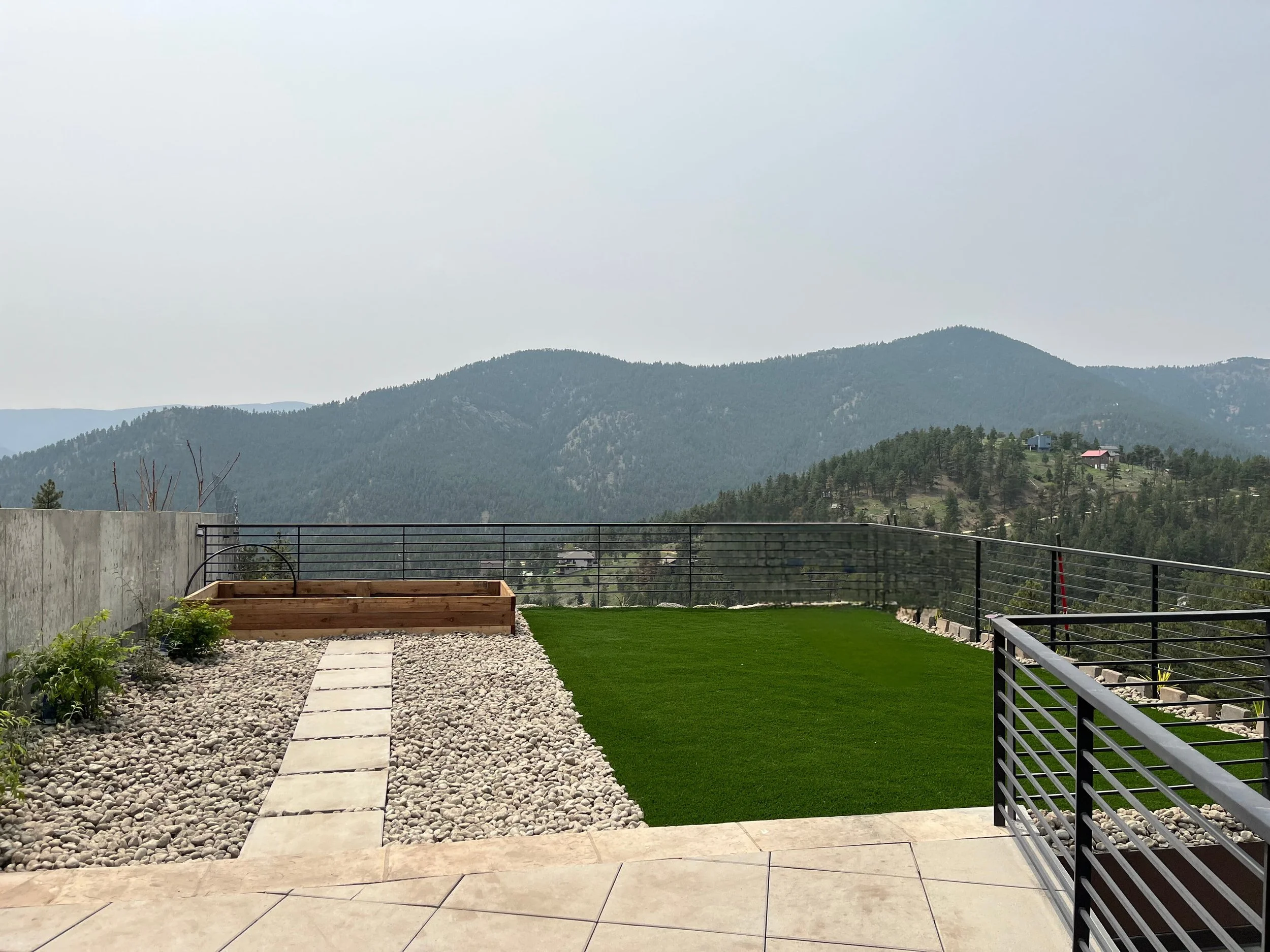View of a rooftop outdoor space with a small grassy area, a stone pathway, and a colorado mountain landscape in the background.