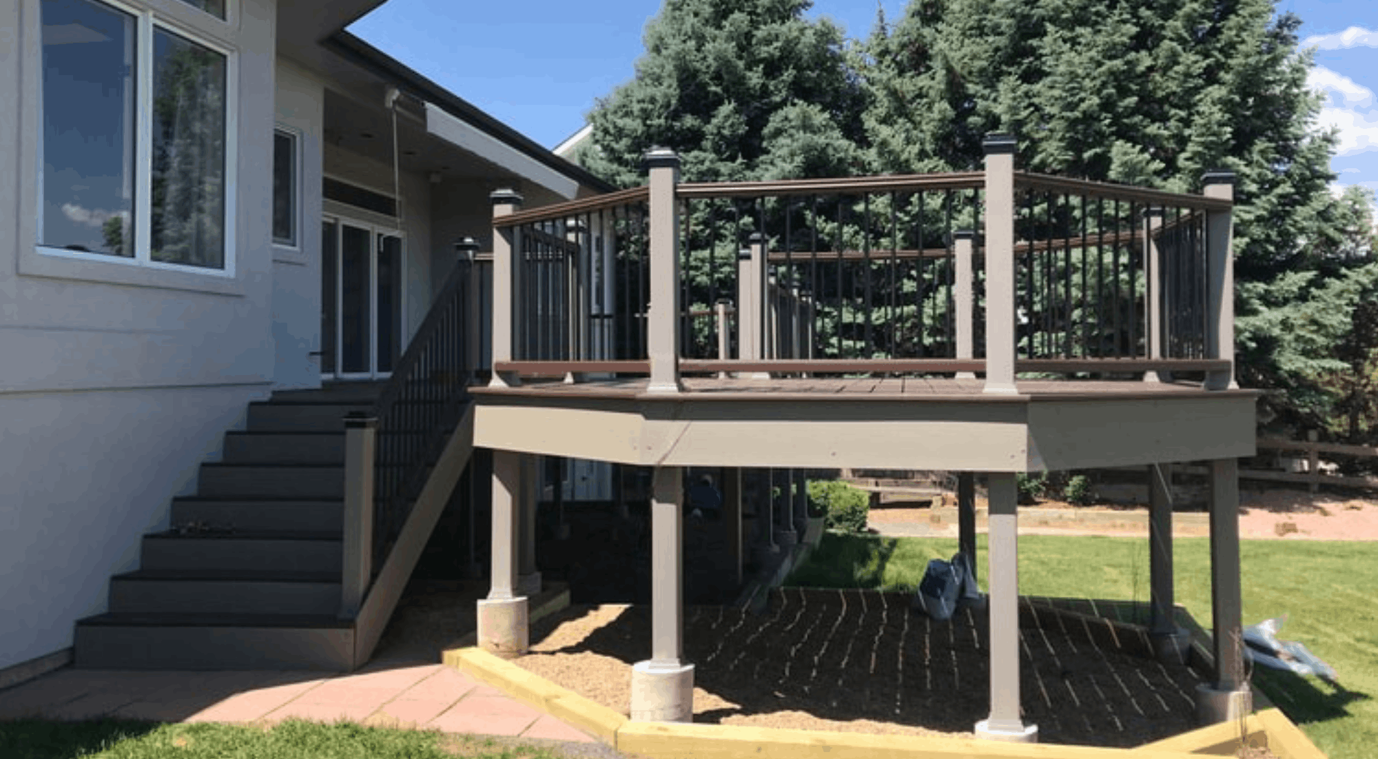 Photo of a house's backyard patio with a newly built trex wooden deck and stairs leading down to the lawn