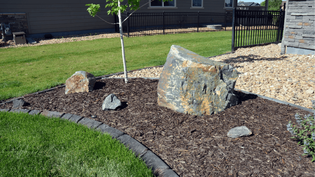 Home garden with landscaped rocks, mulch, and a small tree.