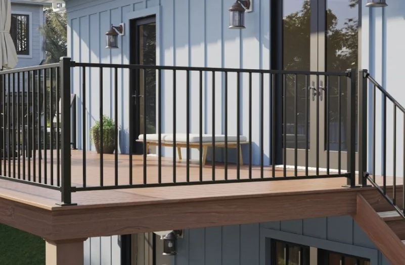 Outdoor wooden deck with black metal railing attached to a house with vertical blue siding, a glass door, and exterior lights.