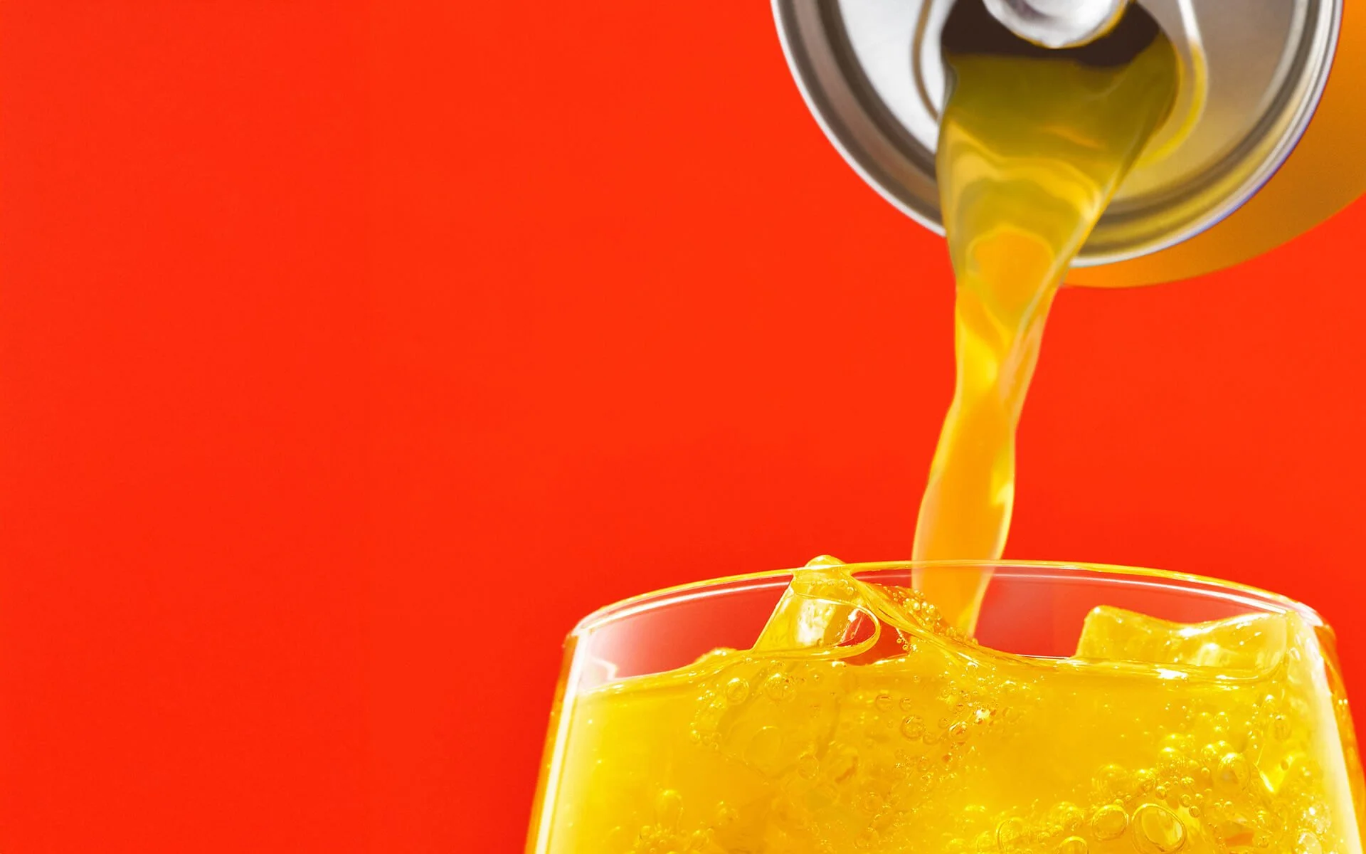 Orange liquid being poured into a glass with ice cubes against an orange background.