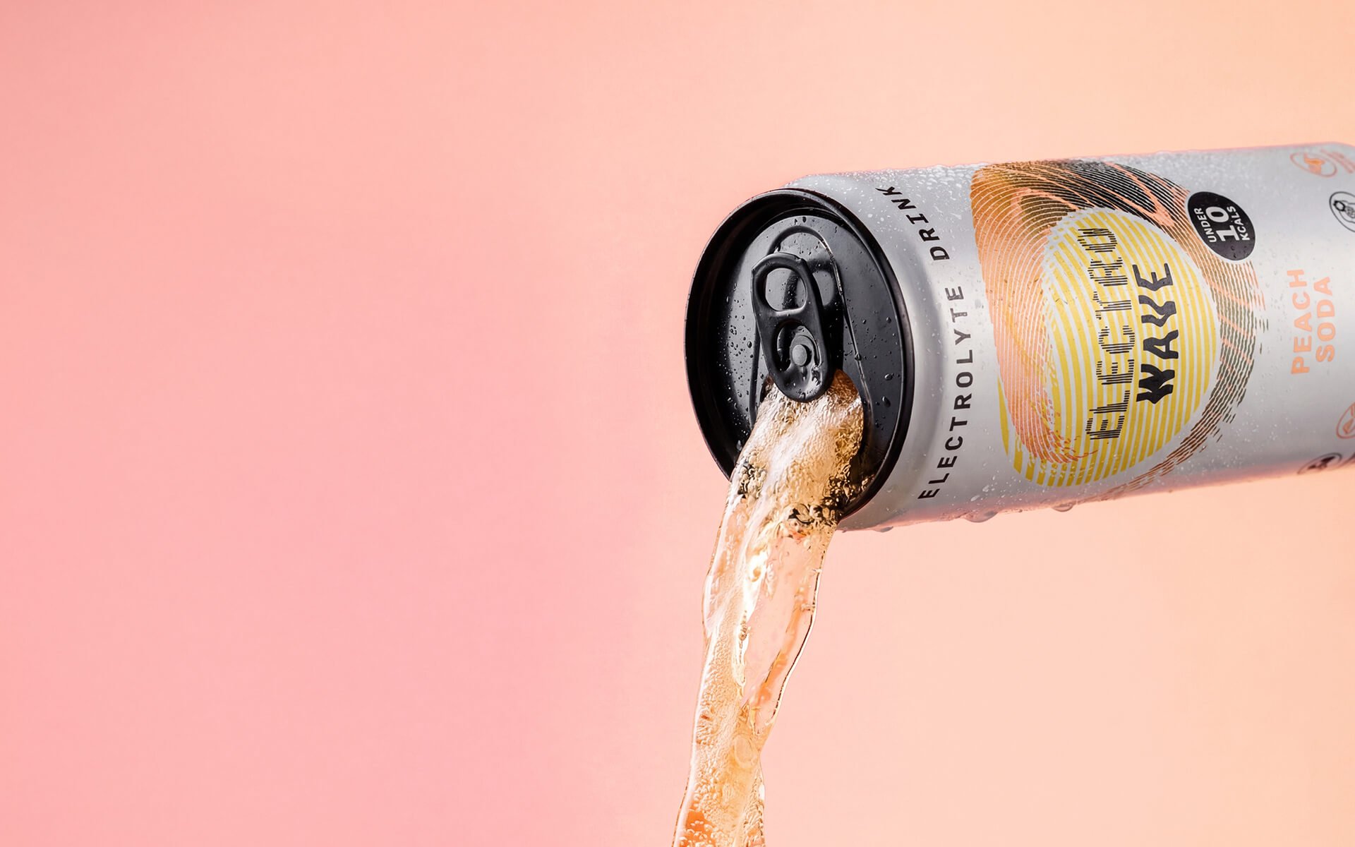 A can of Electric Lime Drink Electric Water Peach Soda tilted, with peach soda flowing out of the opening against a pink background.