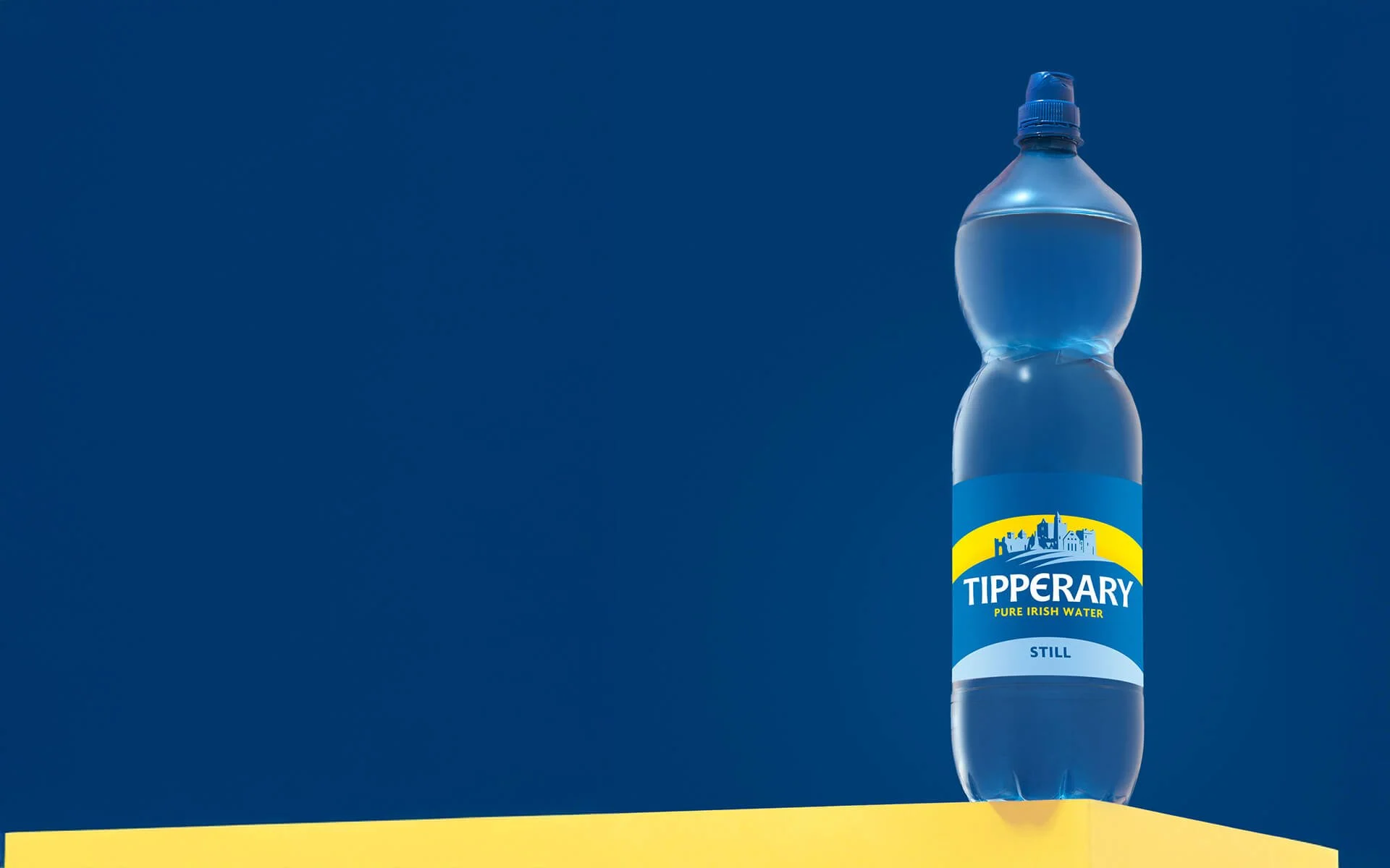 A clear plastic bottle of Tipperary pure Irish water on a yellow surface against a blue background.