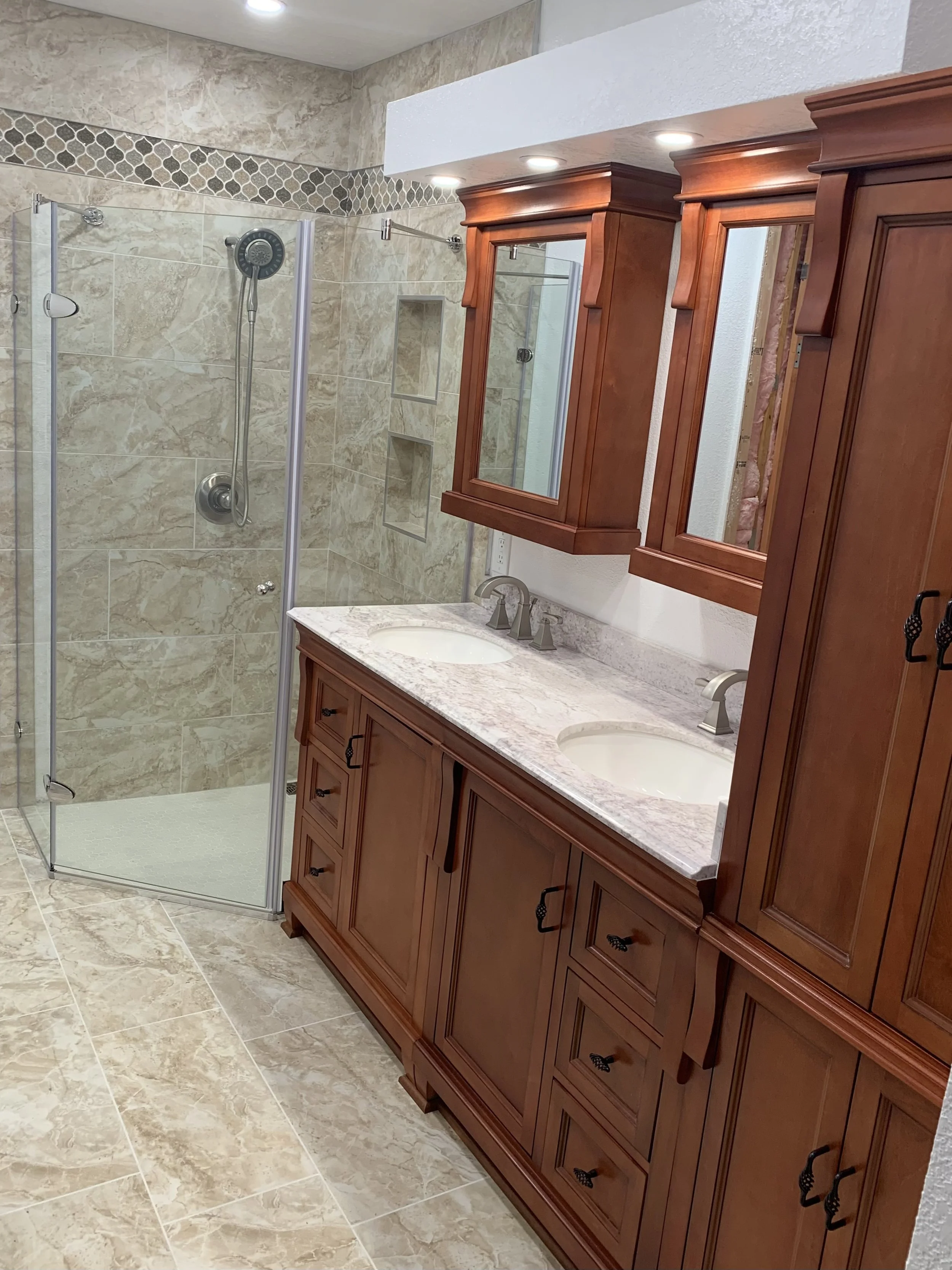 A bathroom with a glass-enclosed shower and a double sink vanity with wooden cabinets and a marble countertop.