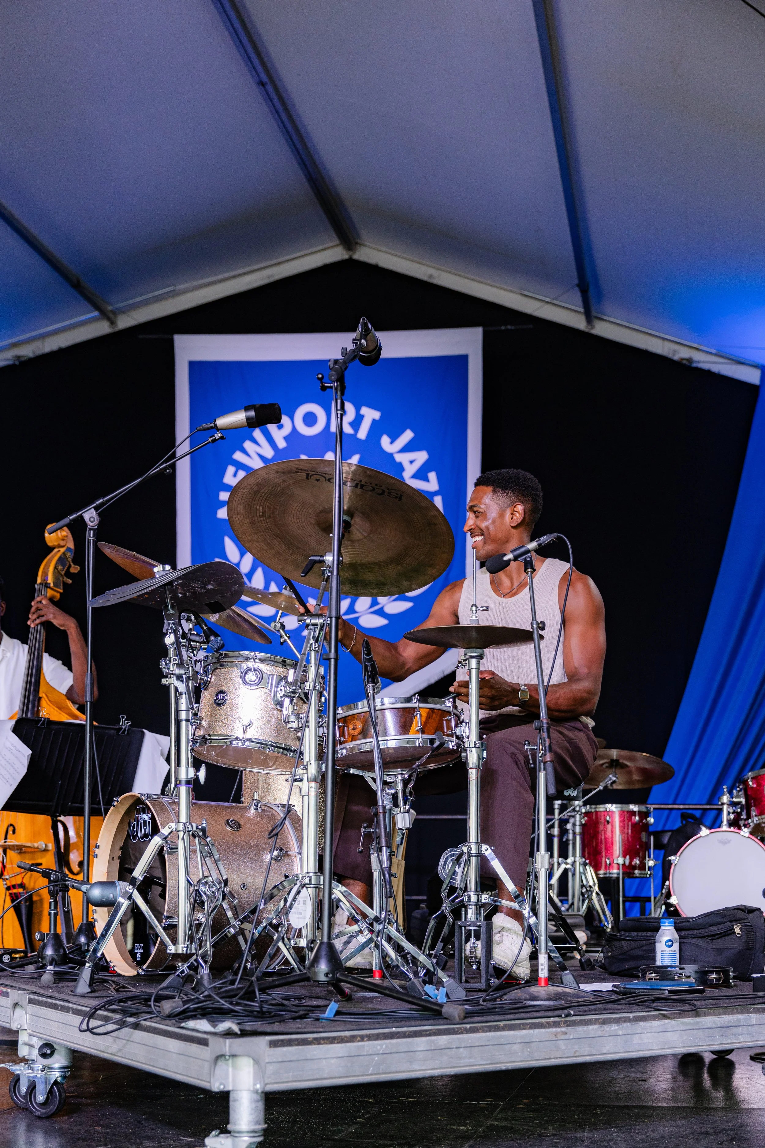 A musician playing drums on stage with a blue and white backdrop for the Hartford Jazz Festival.