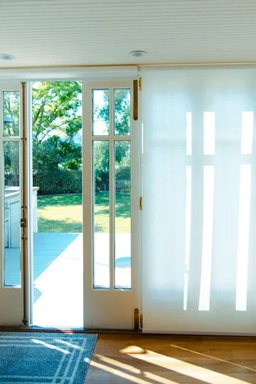 Sunlight streaming through the glass door and windows onto a wooden floor, with a view of a green backyard outside.