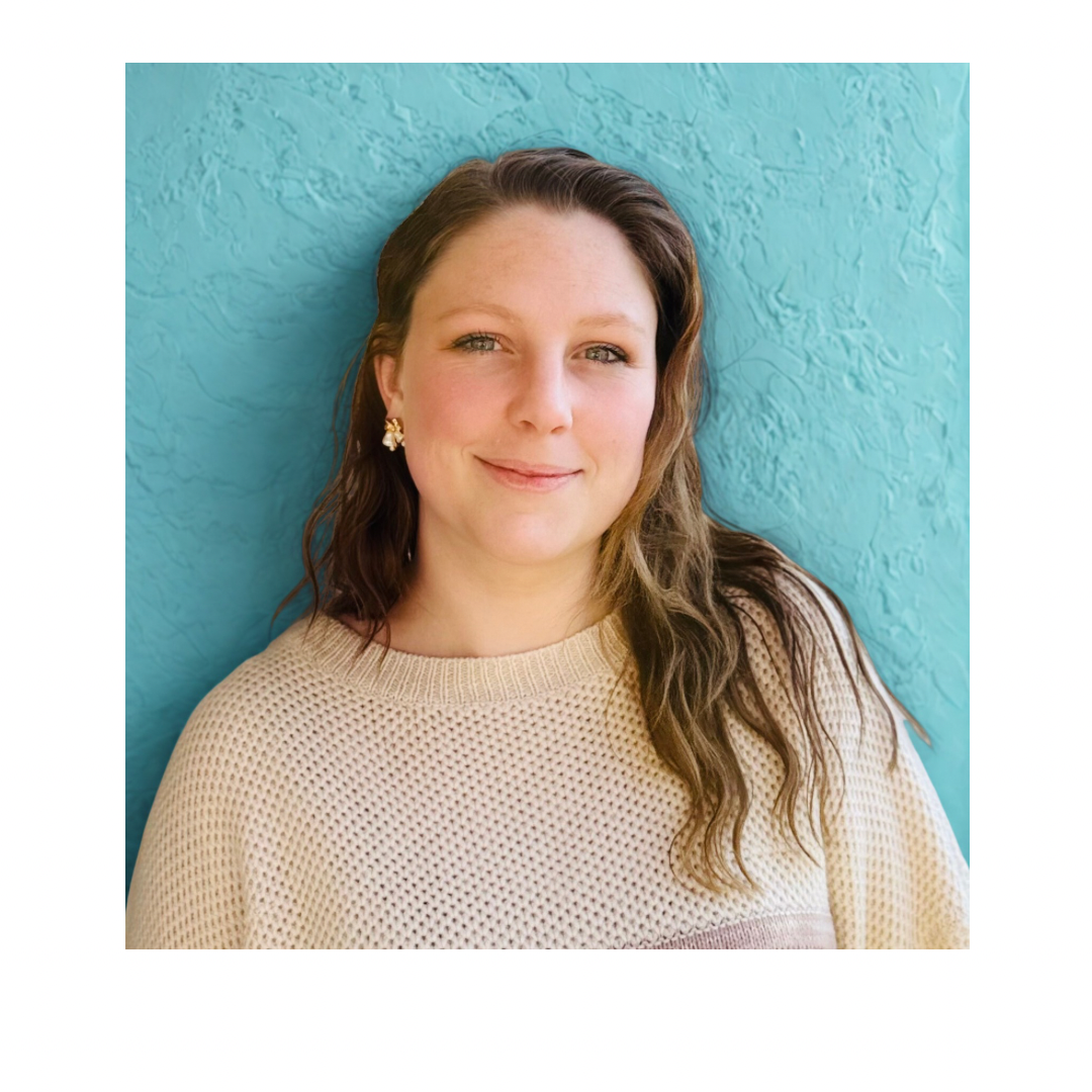 A woman with wavy brown hair smiling against a textured blue background, wearing a beige knitted sweater and gold earrings.