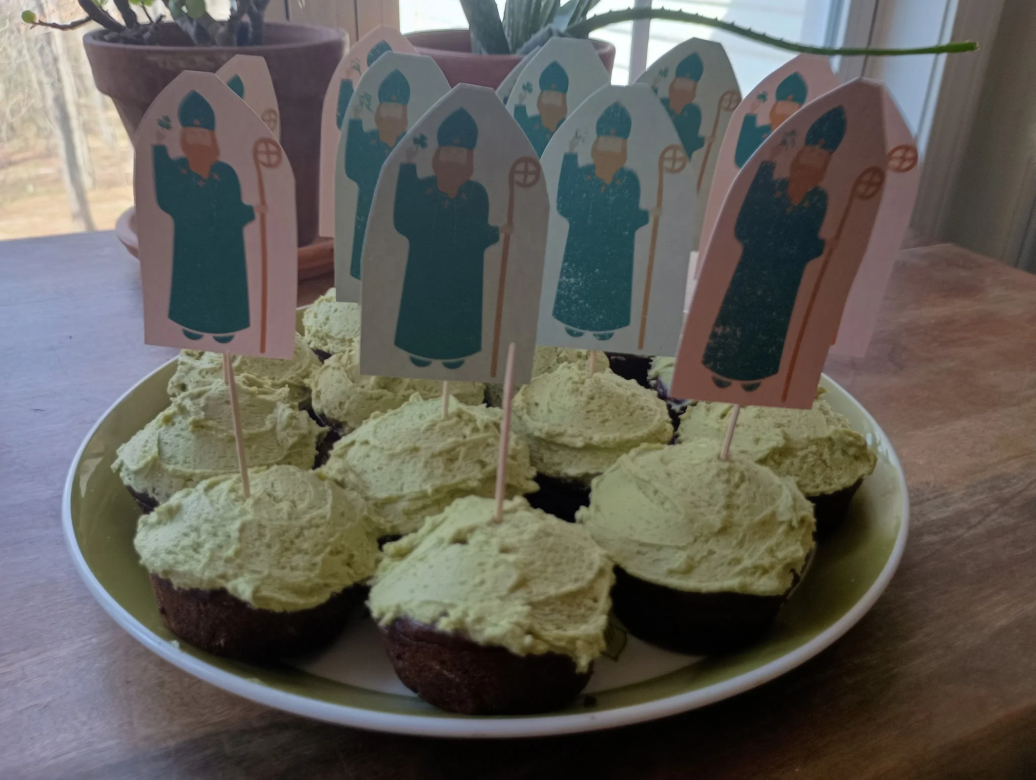 Plate of cupcakes with green frosting and St. Nicholas figurine toppers for Christmas celebration.