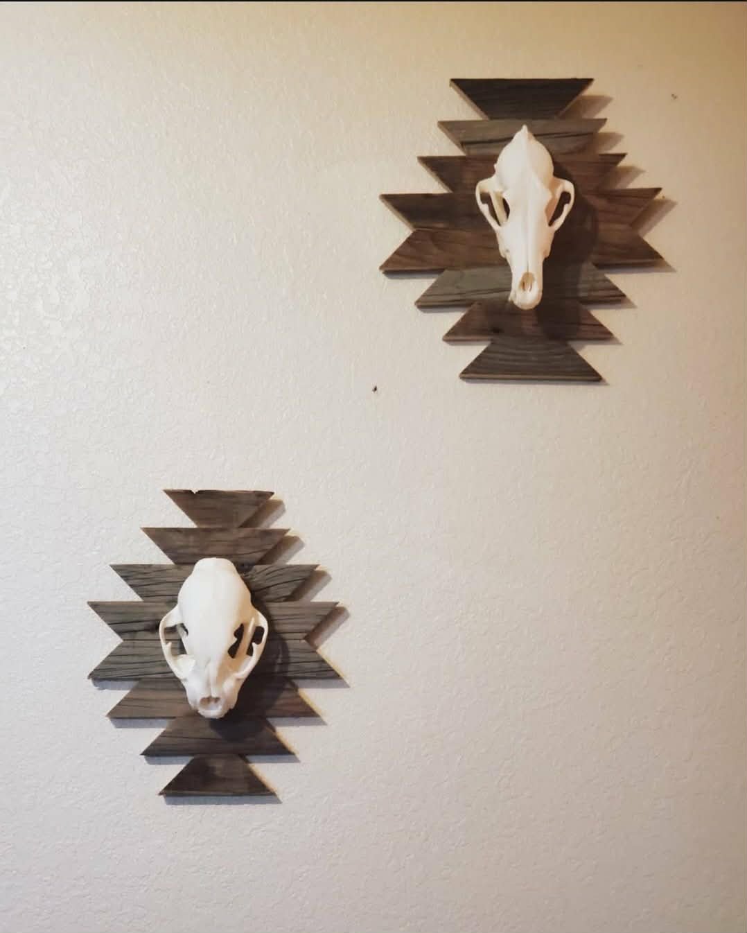 Wall decor featuring two mounted animal skulls, each on a geometric wooden background, arranged in a decorative pattern.