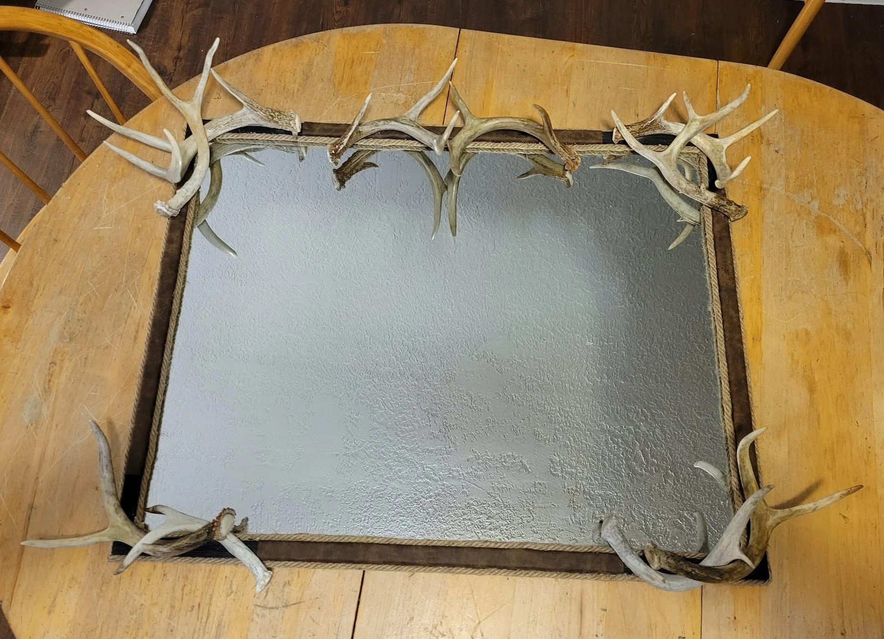A rectangular mirror with a border made of deer antlers, placed on a wooden table.