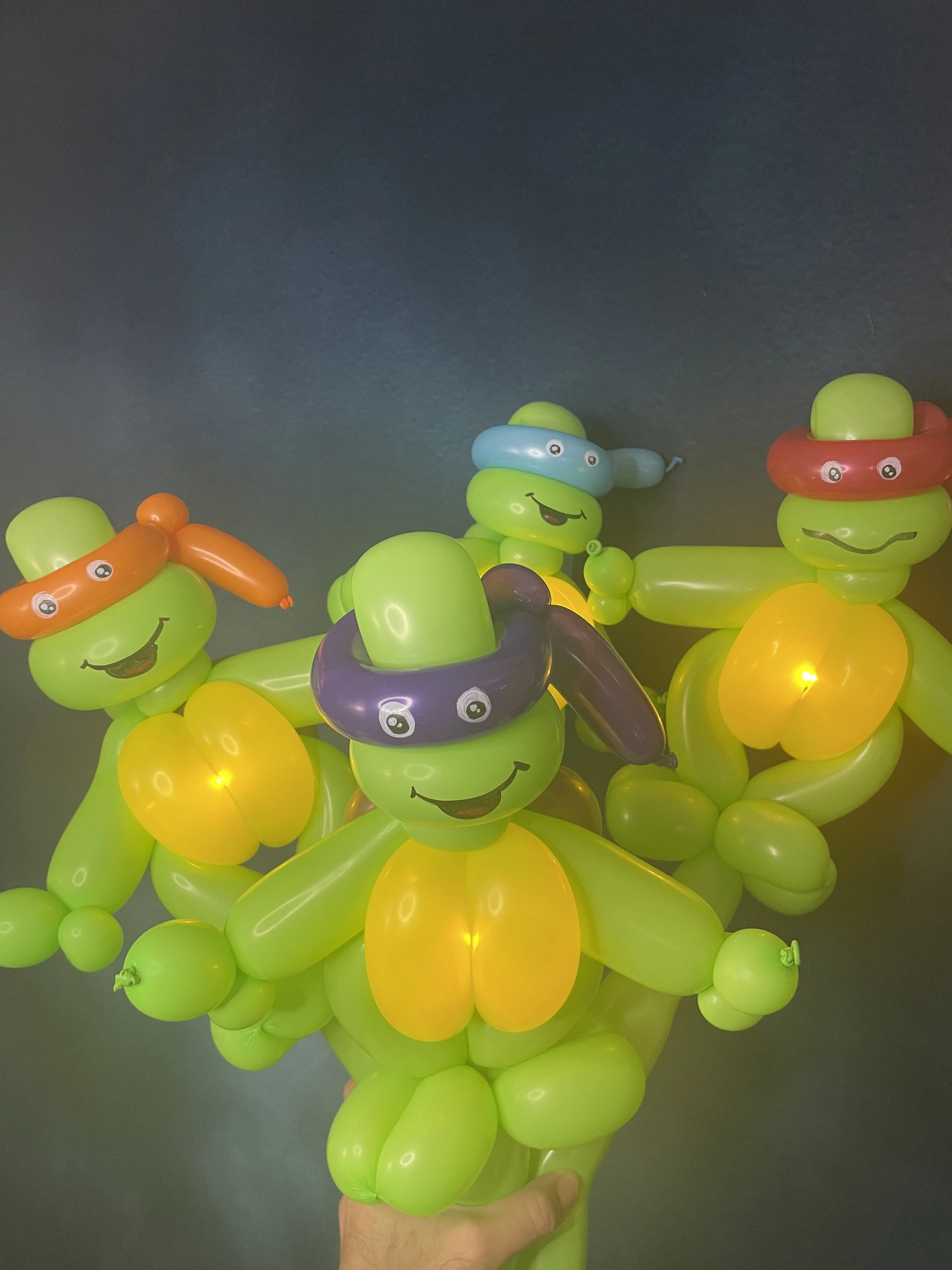 Colorful balloon art depicting turtles with smiling faces wearing sunglasses, arranged to resemble turtle shapes.
