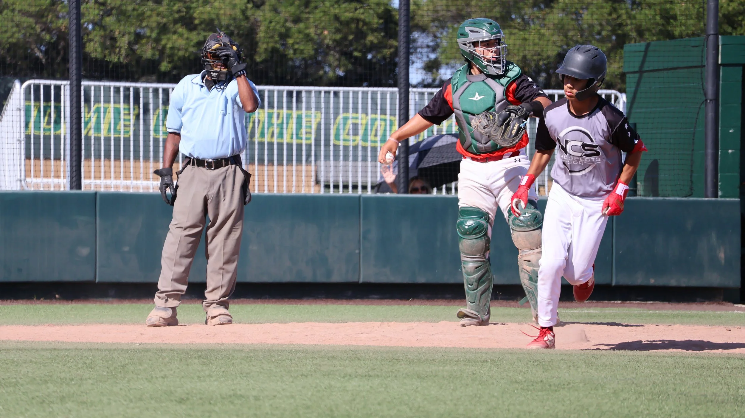 A young baseball player is running near home plate as the catcher and an umpire stand nearby on the field.