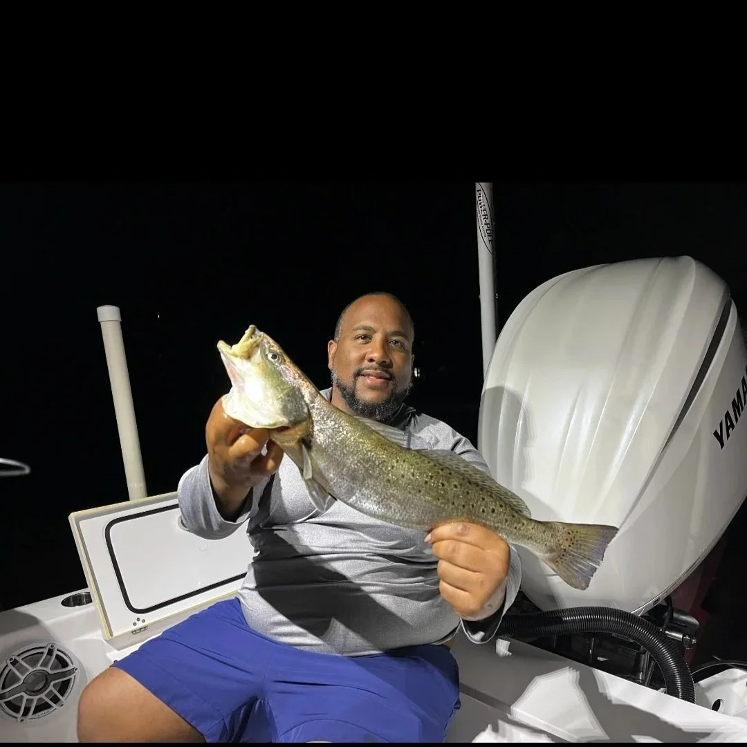 A man sitting in a boat at night holding a large fish he caught.