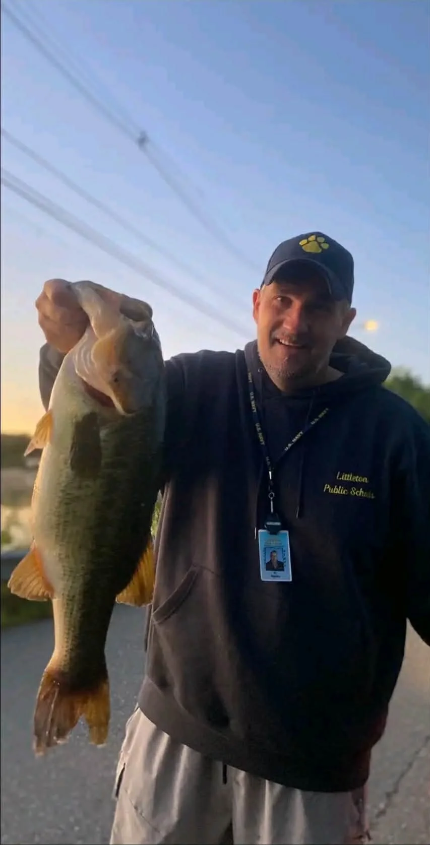 Backwater customer holding a large bass fish outdoors during sunset, smiling,