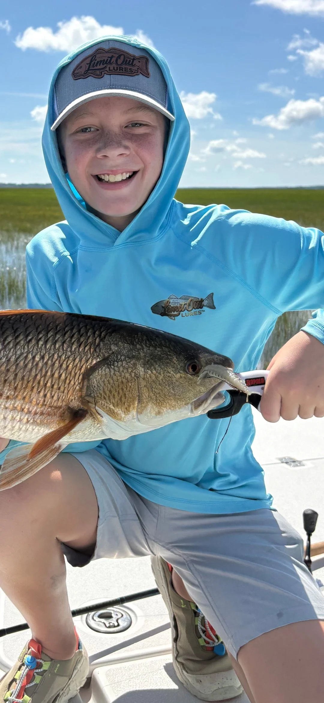 Kid-holding-a-redfish-he-caught-using-3-inch-hellgramite-in-florida-flats-wearing-limit-out-lures-hat-and-shirt