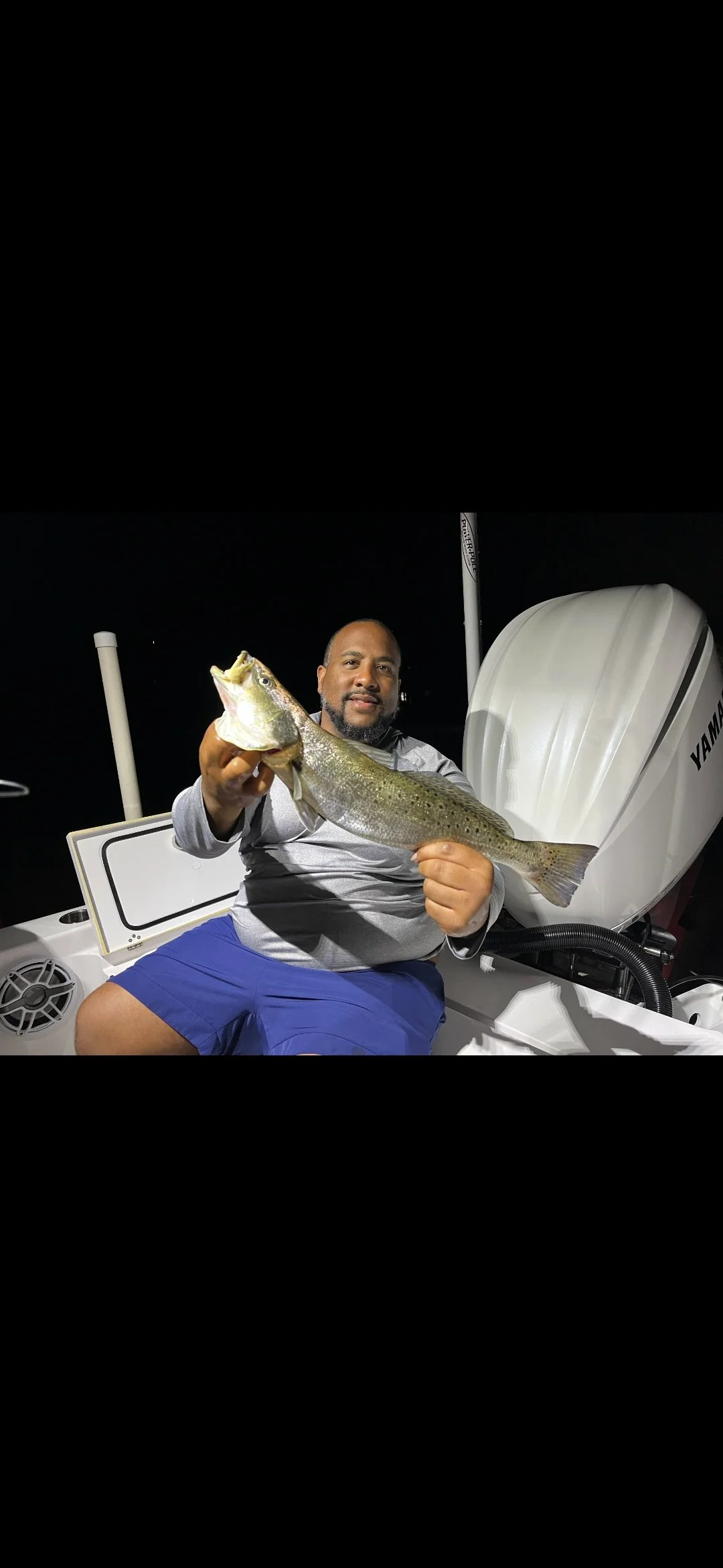 A man sitting in a boat at night holding a large fish he caught.
