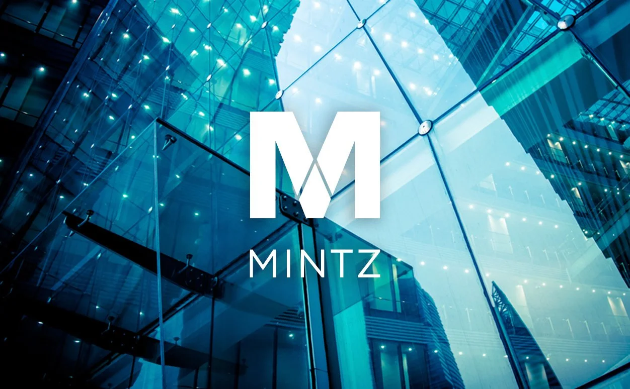 Modern glass building with reflections and lighting, featuring the Mintz logo in the center.