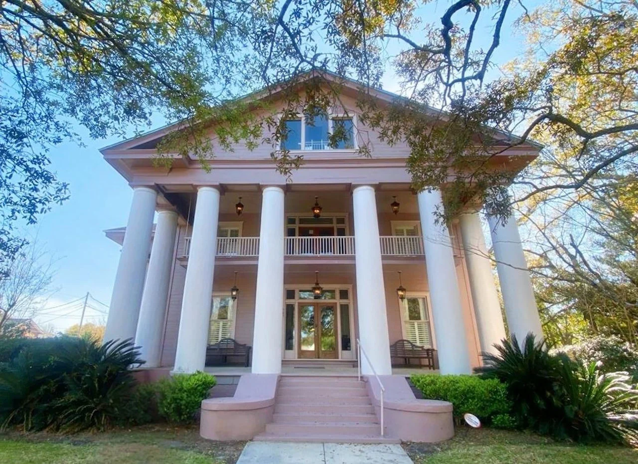 The Amason House, a two-story pink historic mansion featuring white columns and a central balcony