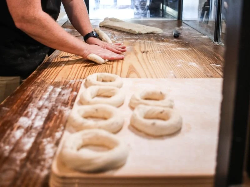 a baker shaping dough into ring-shaped bagels on a floured wooden counter