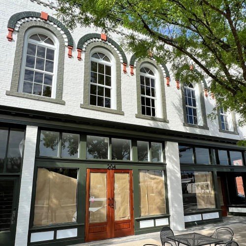 A white brick building with arched windows and dark green trim, featuring a red wooden double door