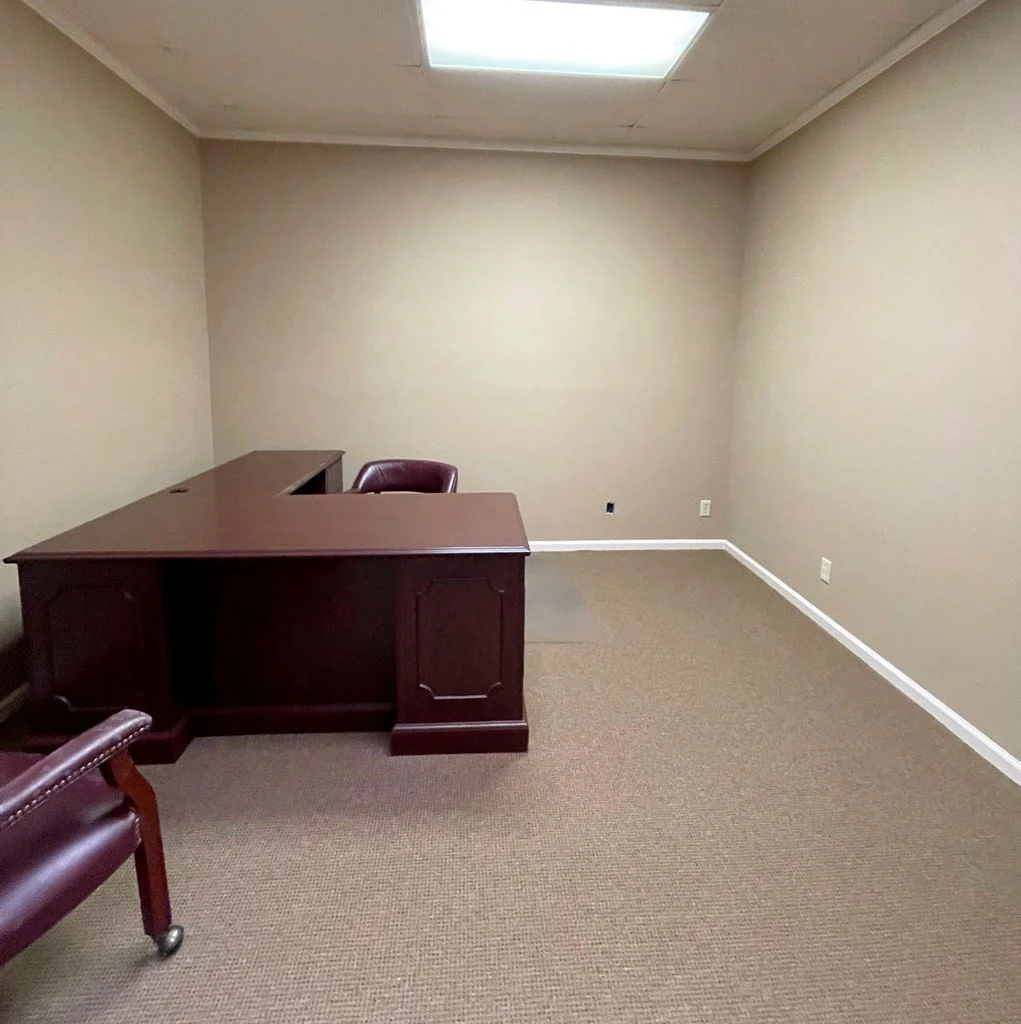 An office with a traditional L-shaped mahogany desk with matching leather chairs