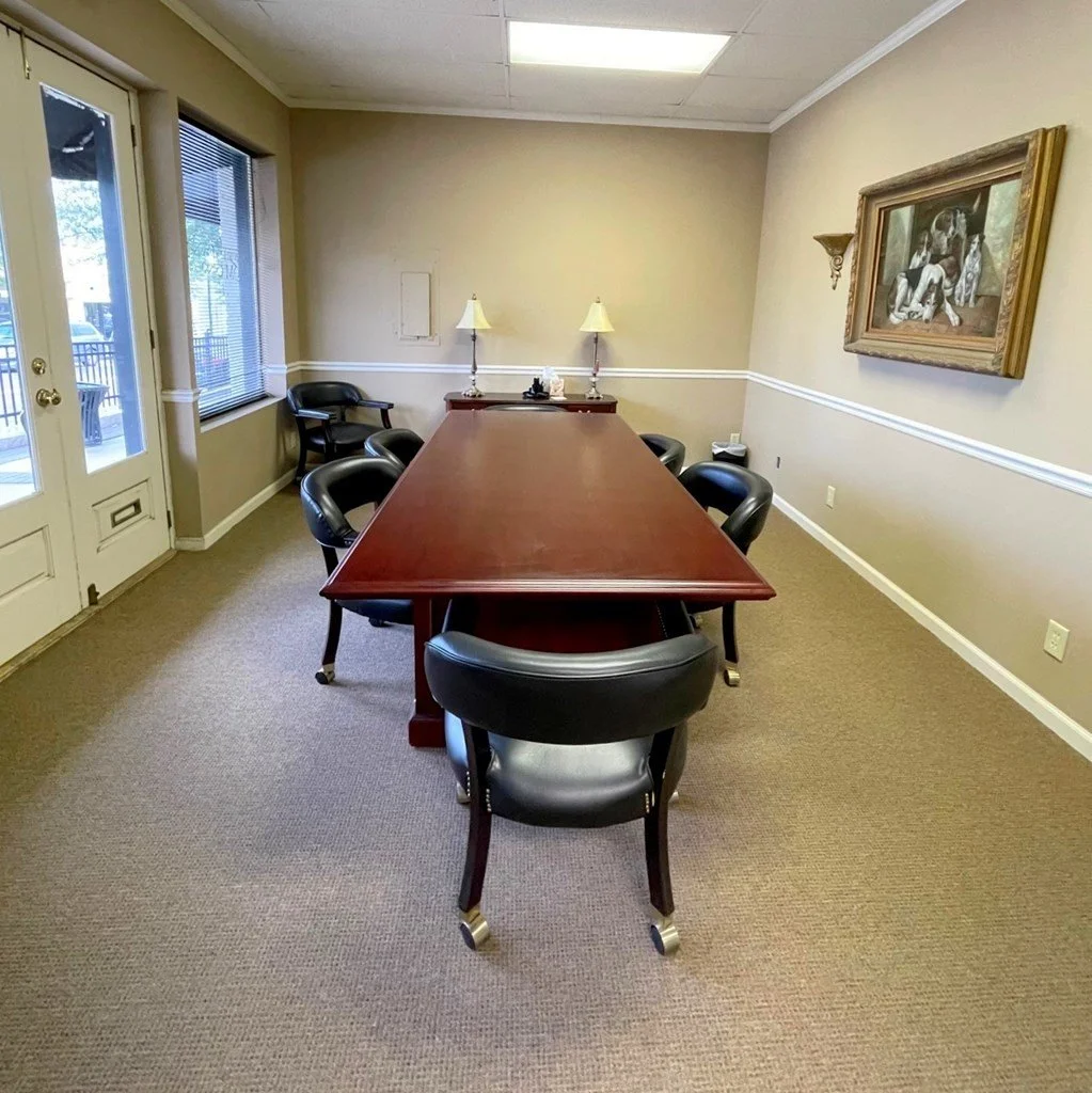 A professional conference room featuring a large, polished wood table and black leather chairs
