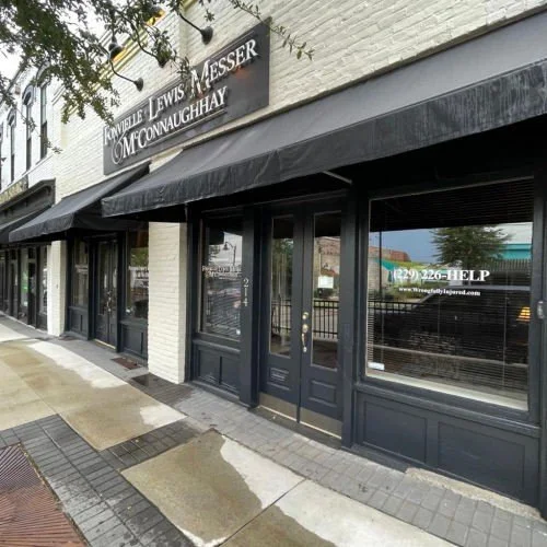 Exterior of a law office with a black awning, glass doors, and a window phone number