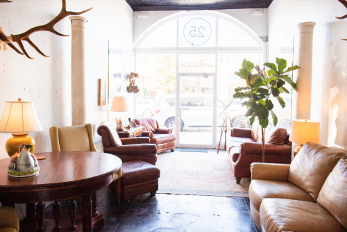 A sunlit office lounge with leather chairs, sofas, a round table, large plants, and arched windows